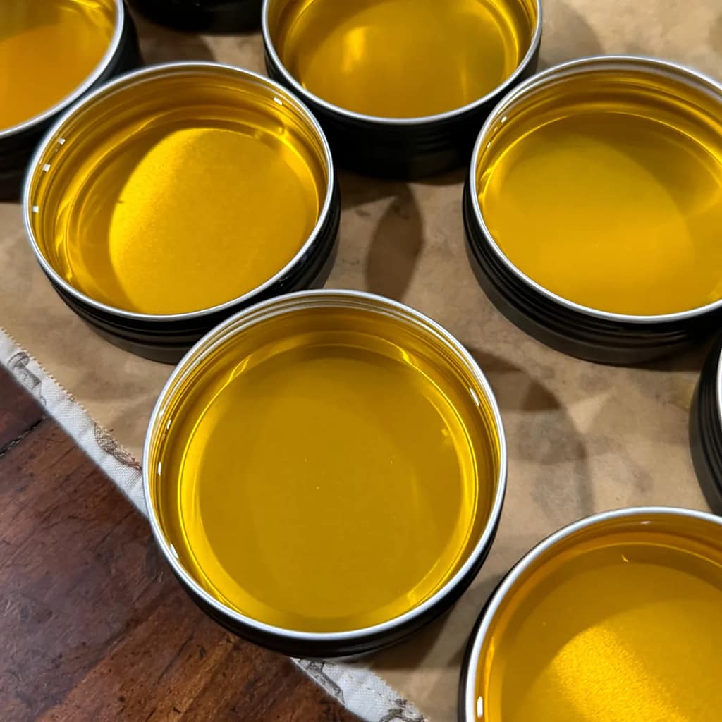 Close-up of open tins filled with golden liquid hand salve before it sets.