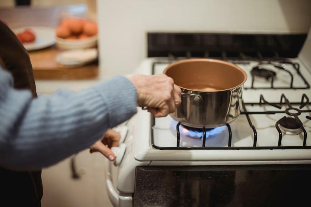 A woman cooks using a saucepan on a modern gas stove indoors, showcasing domestic kitchen activity.