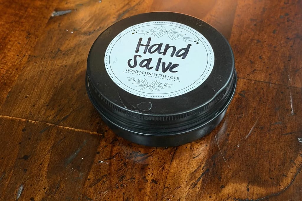 Closed tin of homemade hand salve with a printed “Hand Salve” label on a wooden tabletop.