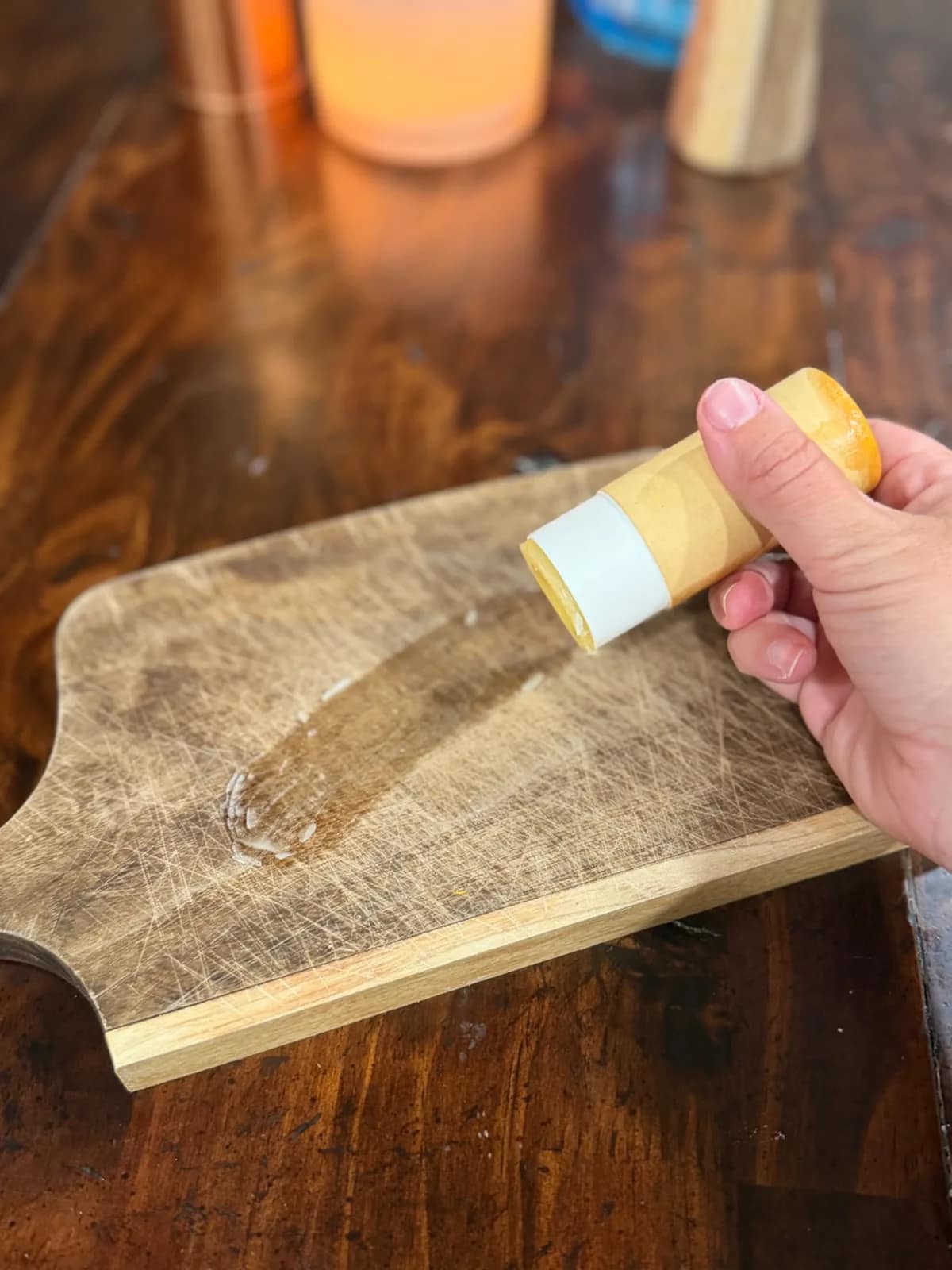 Hand holding a cutting board balm tube above a wooden board