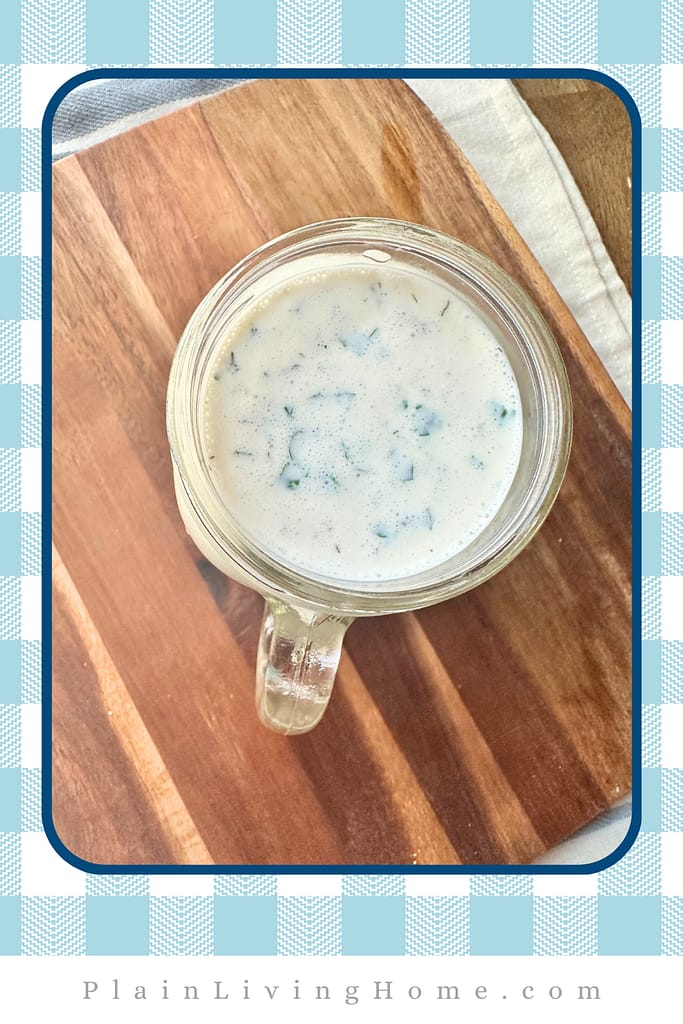 looking down into a mason jar full of homemade ranch, a creamy sauce with herbs and spices 