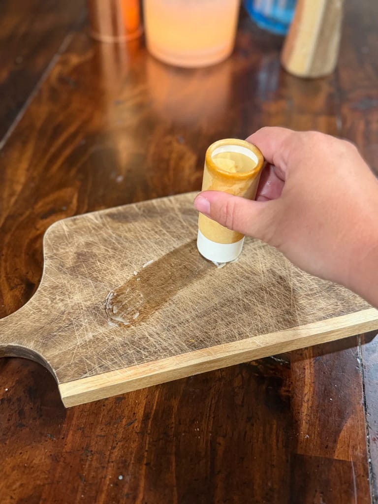A hand applying a cutting board balm stick directly to a wooden board