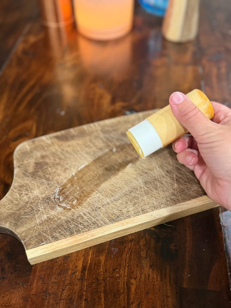 Hand holding a cutting board balm tube above a wooden board