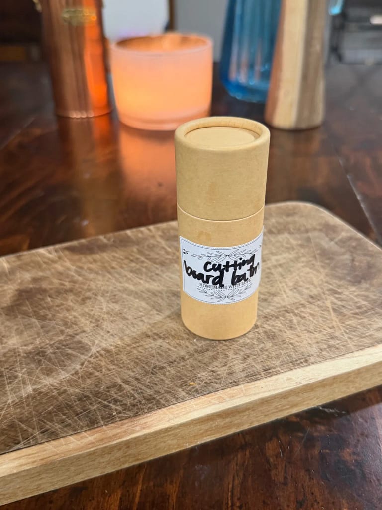 Homemade cutting board wax in a paper push-up tube on a wooden cutting board