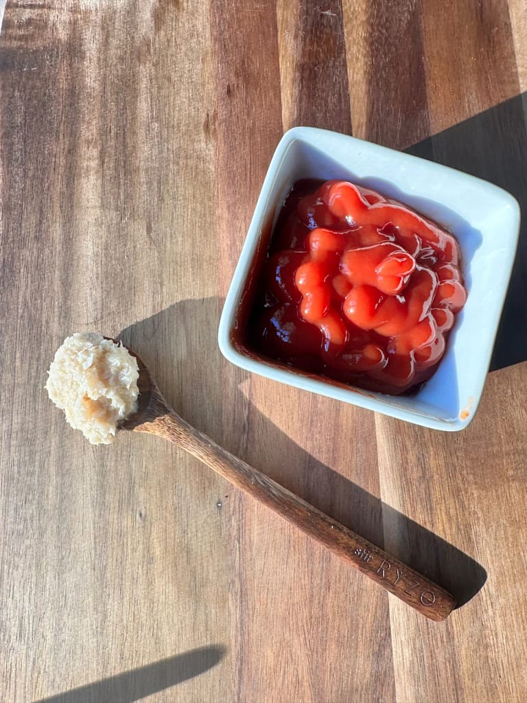 Ketchup in a white bowl beside a wooden spoon filled with grated horseradish.