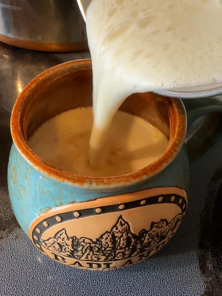 Homemade white hot chocolate being poured into a turquoise mug