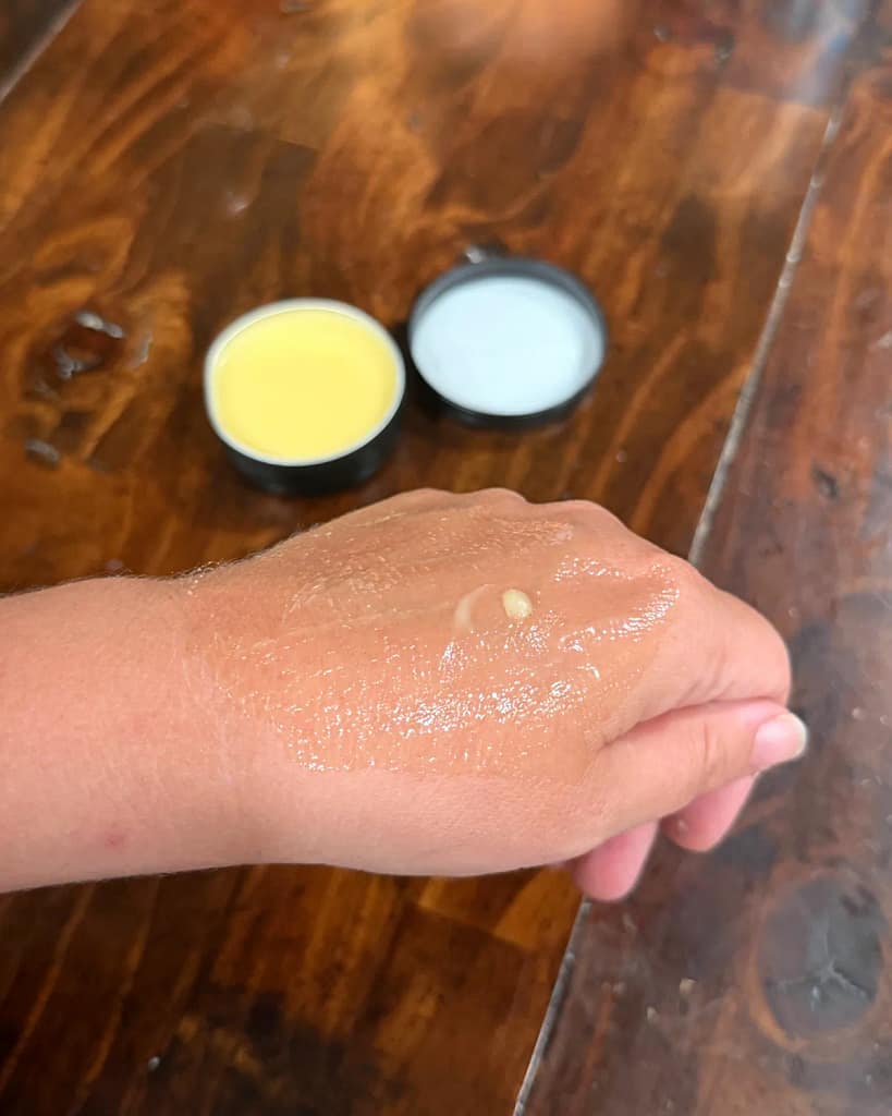 Hand salve spread across the back of a hand, with the open tin and lid in the background.