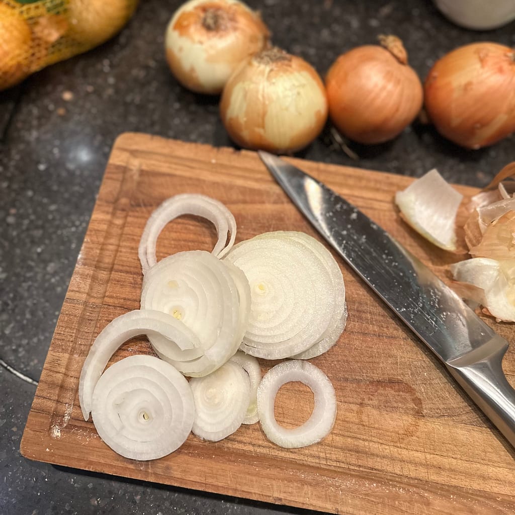 kitchen knife on a cutting board with slices of onions