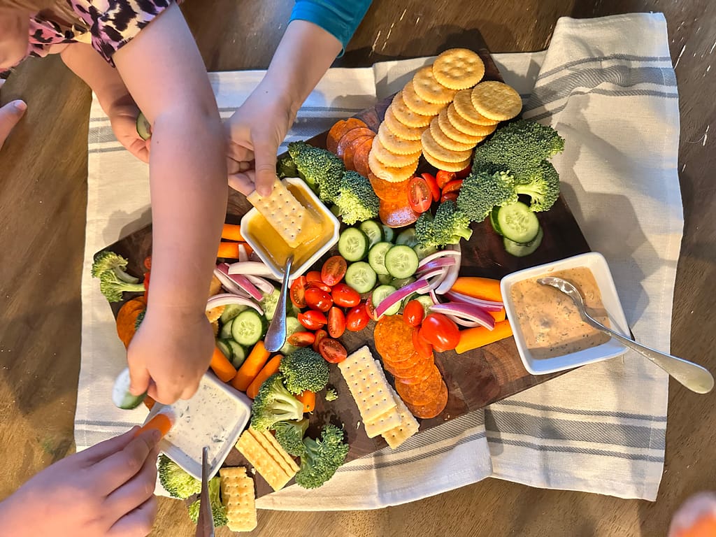 a beautiful fresh veggie tray with homemade ranch, honey mustard, and thousand island, with kids eating the snacks and dip