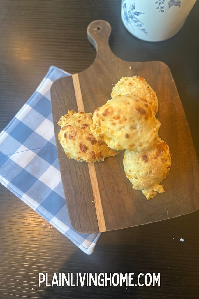 sourdough cheddar biscuits stacked on a wood cutting board, with a blue plaid hot pad underneath