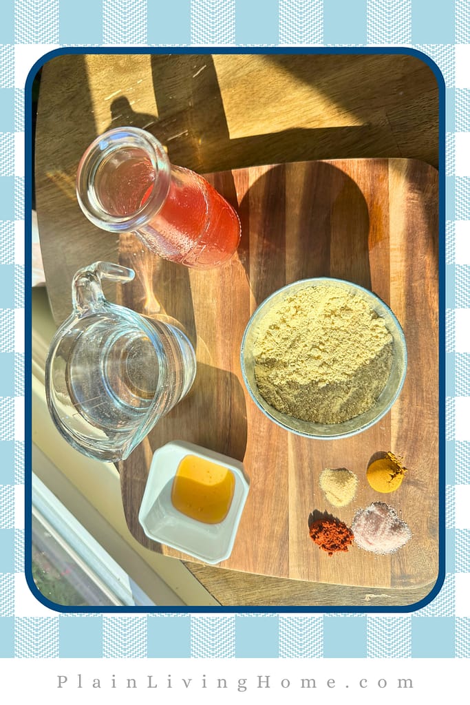 red wine vinegar, water, mustard powder, honey, paprika, garlic powder, salt, and turmeric powder lined up on a wooden tray in the sunlight in preparation for making homemade mustard
