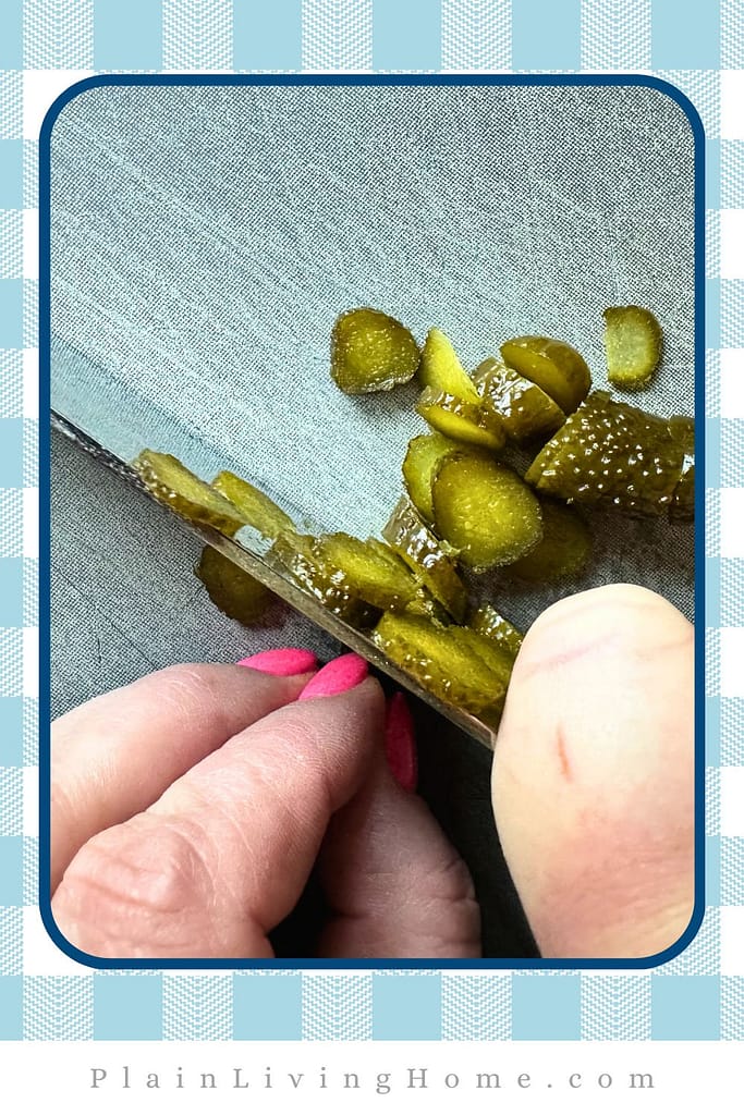 a chef, holding a large knife, carefully chopping up pickles to add to homemade thousand island dressing